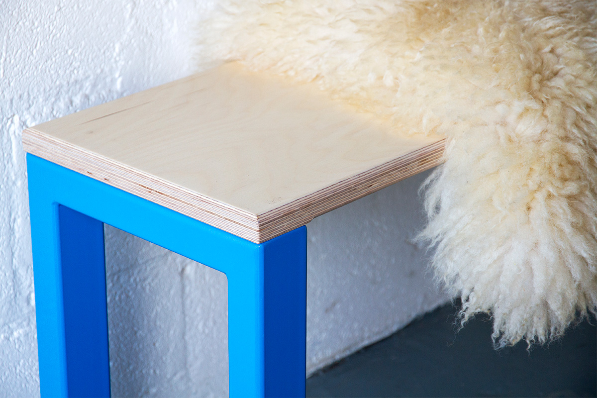 nola bench with blue legs and a birch ply seat, covered with a sheppskin throw