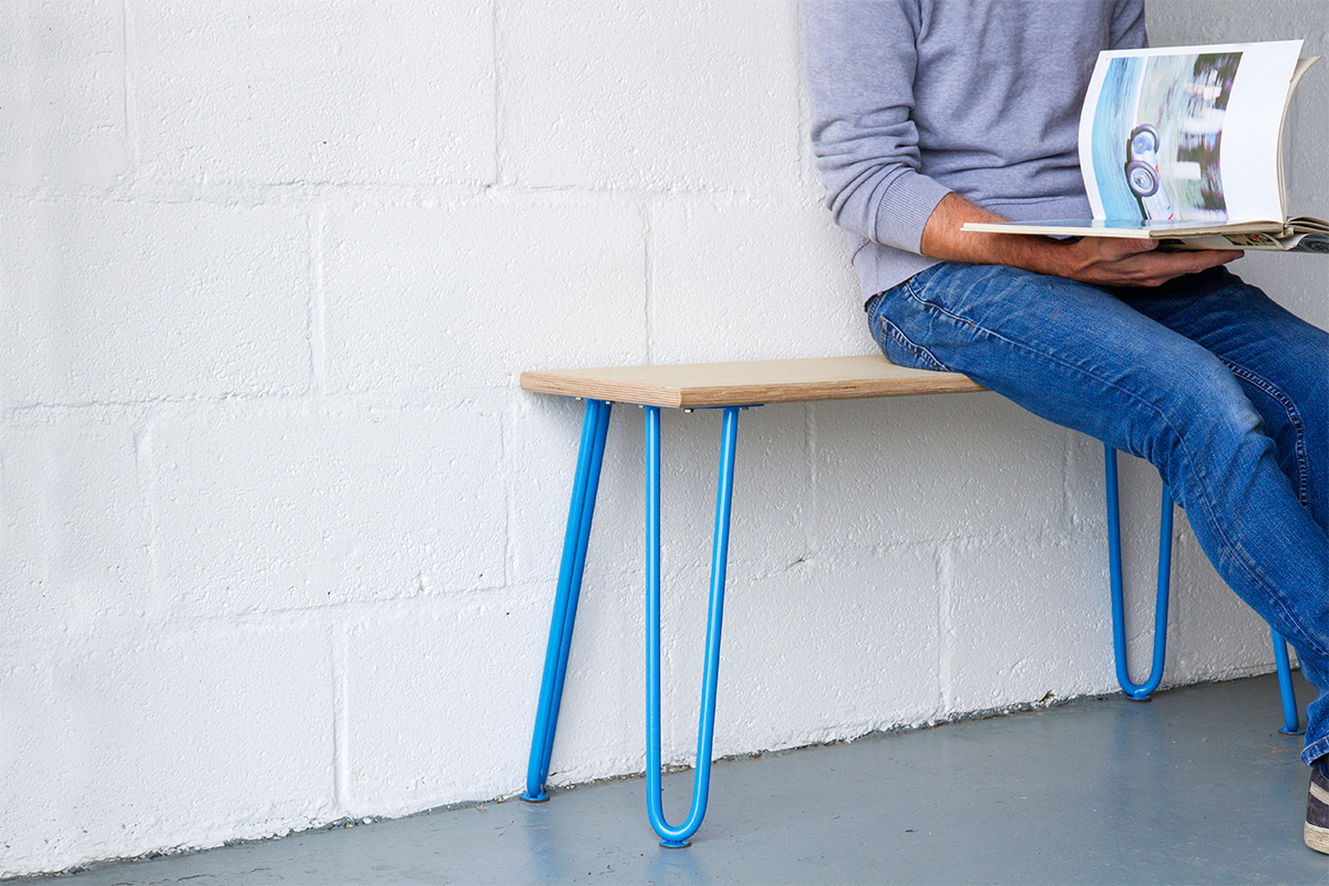man reading a book sat on a hairpin leg bench with blue legs and plywood seat