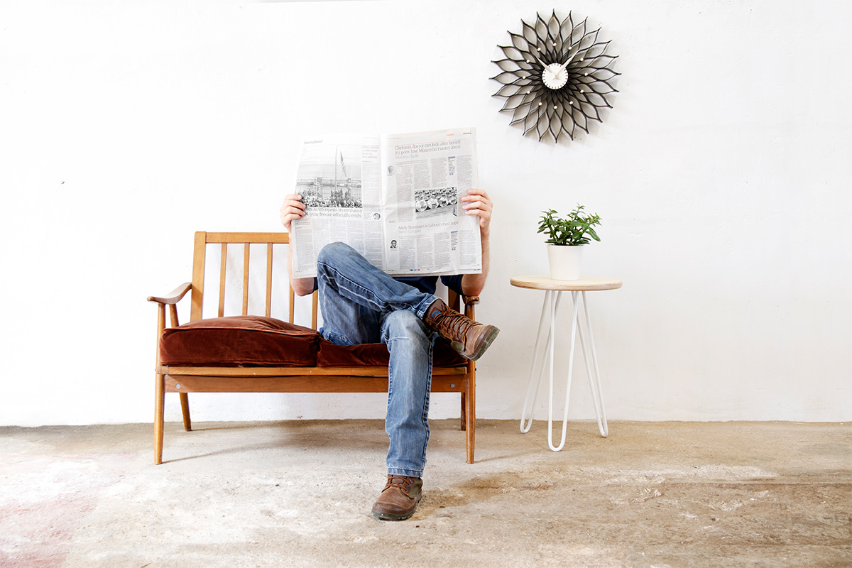 person sat reading a newspaper next to a hairpin leg side table with house plant on it