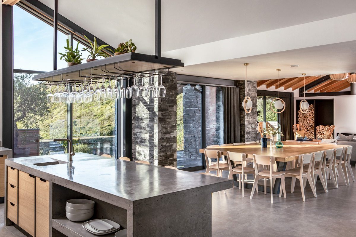 open plan kitchen with poured concrete kitchen island and hanging glass rack 