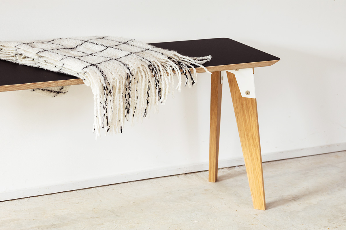 modpop bench with black bench top sea, white steel brackets and solid oak legs, with a throw draped over it