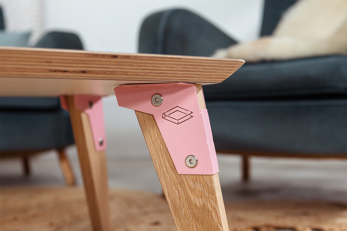 edge detail of a modpop coffee table with white fenix top, pink brackets and solid oak legs.