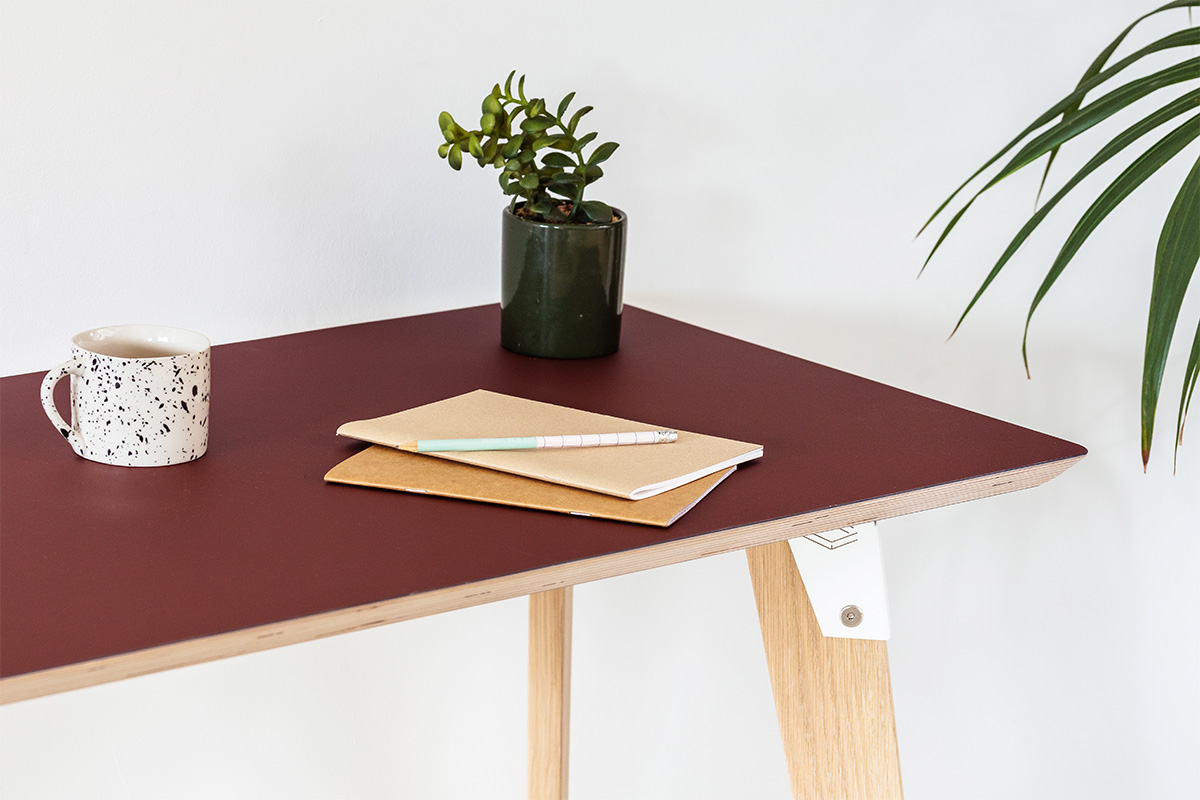 corner detail of modpop desk with rust red Fenix desk top, white brackets and solid oak legs