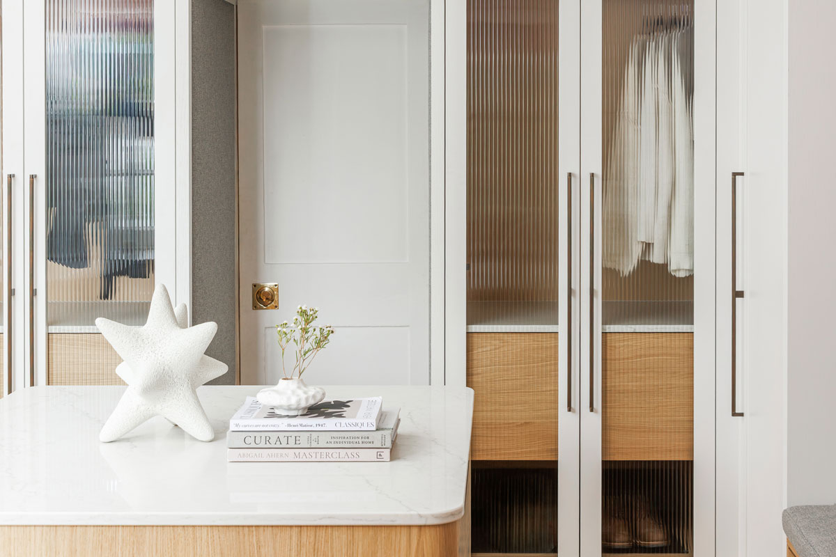 Bespoke wardrobes in a one off walk-in wardrobe with central island in oak with fluted glass and marble tops